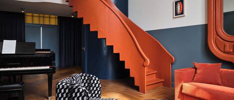 Una habitación con un piano, una escalera, un sofá y una mesa de centro.