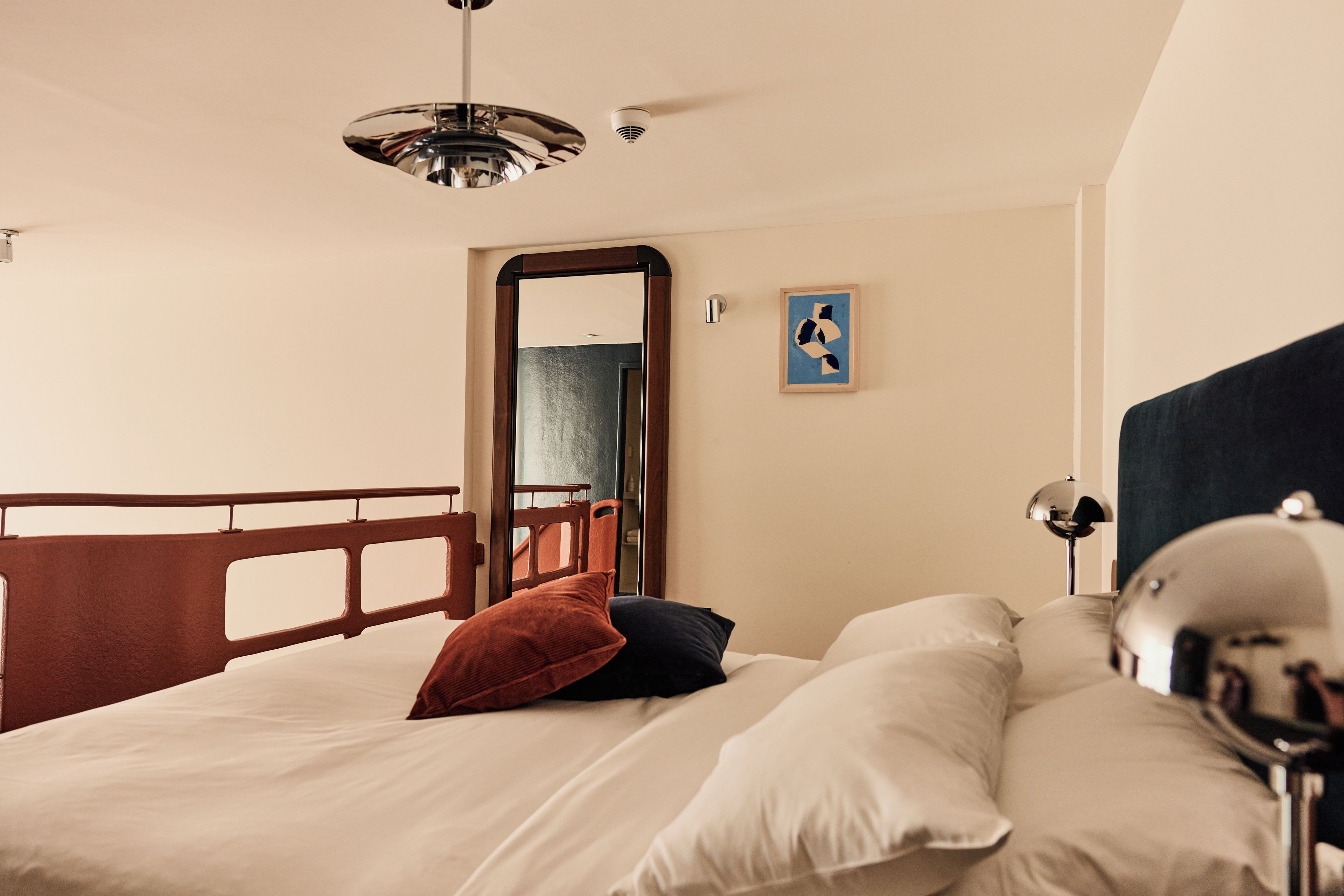 A hotel room with a bed, a bedside table, a lamp, and a mirror.