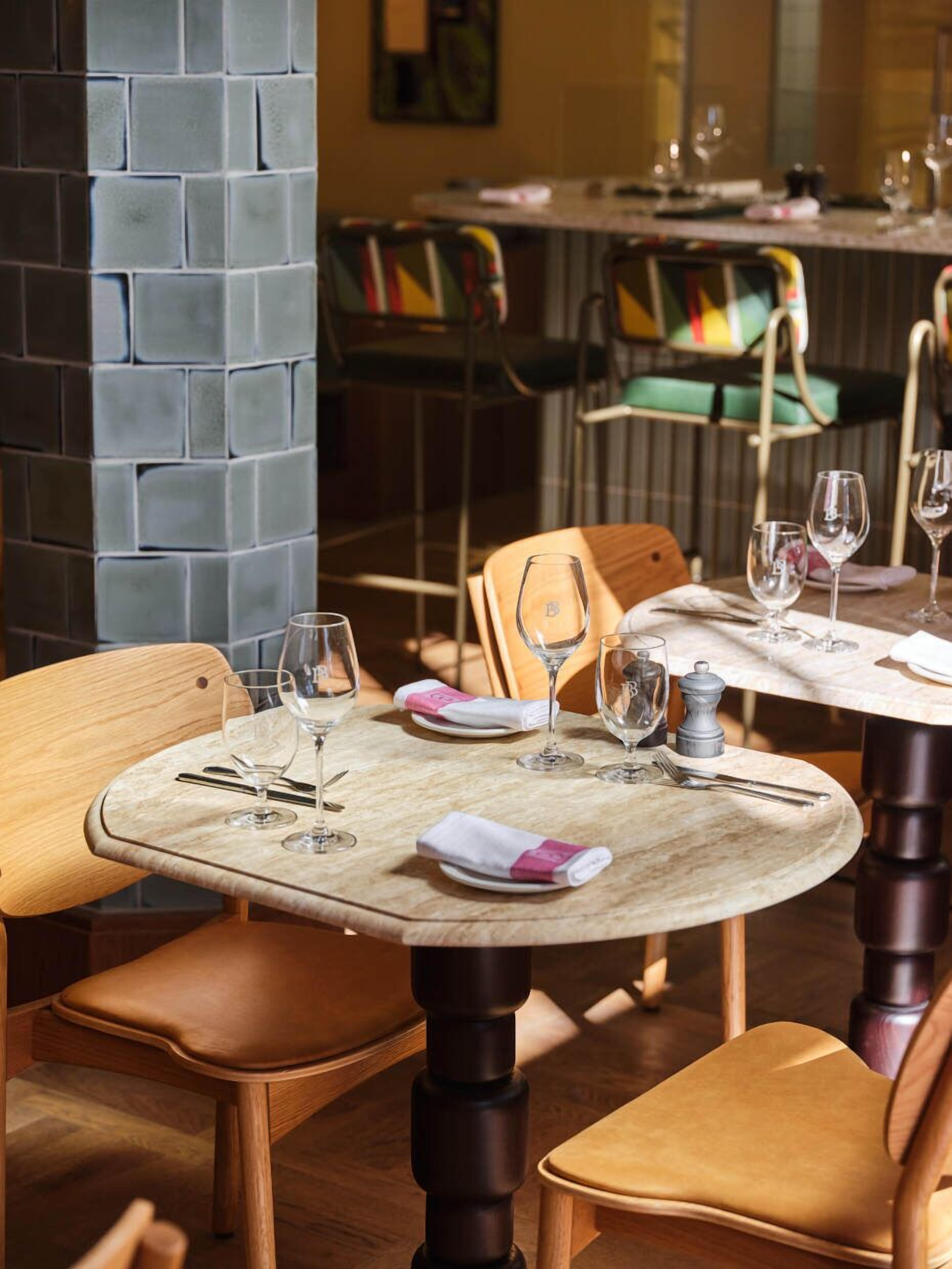 Un interior de restaurante con mesas redondas, sillas de madera y una pared de ladrillo.