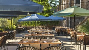 Un área de comedor al aire libre con mesas y sillas, protegida por sombrillas.