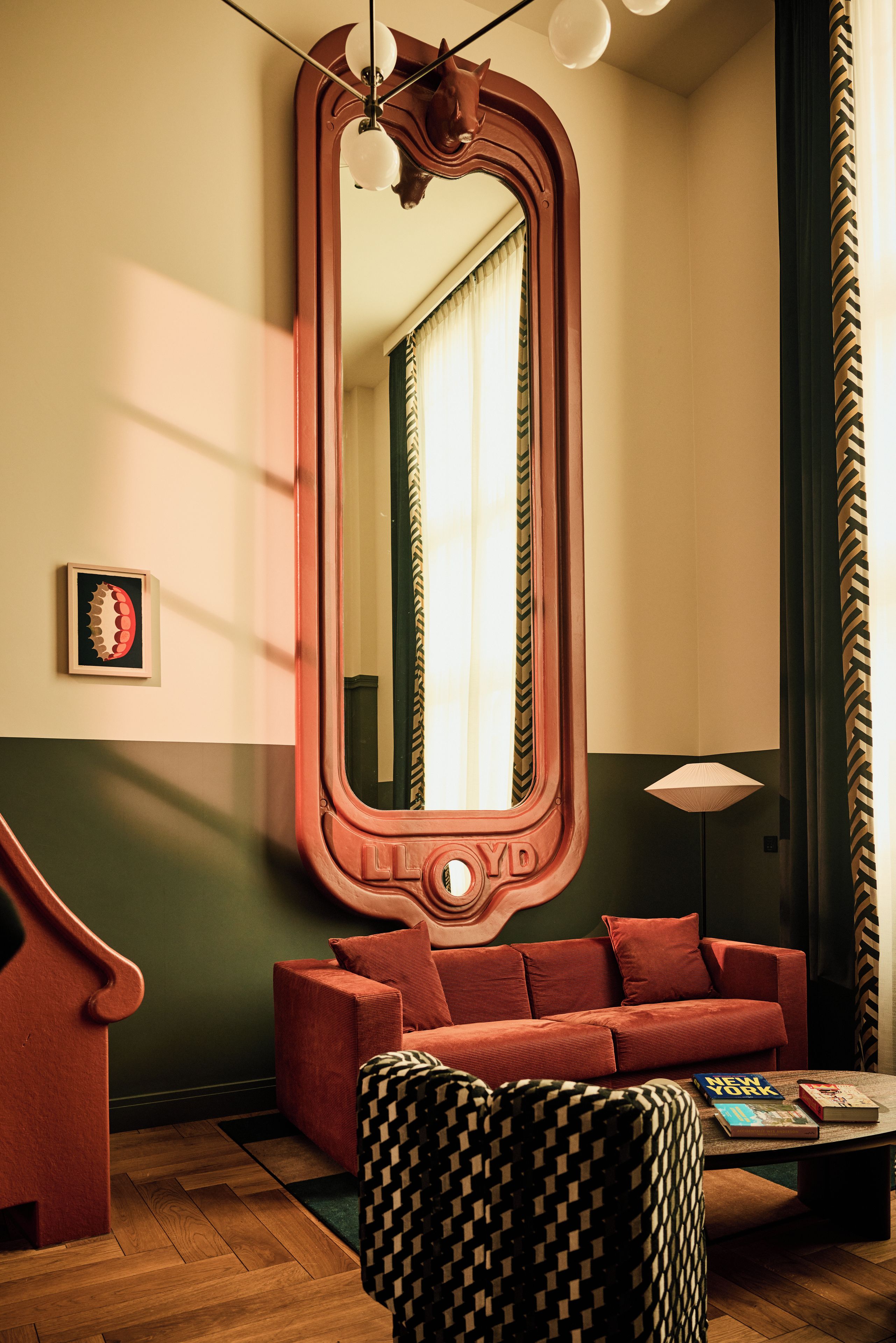 A room with a large mirror, a red sofa, a patterned ottoman, and a floor lamp.