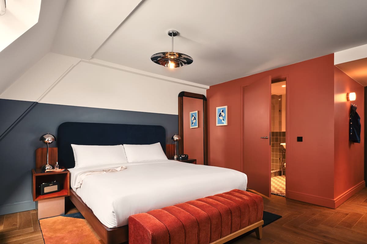 A modern hotel room with a large bed, a bench, a nightstand, a mirror, and a ceiling light.