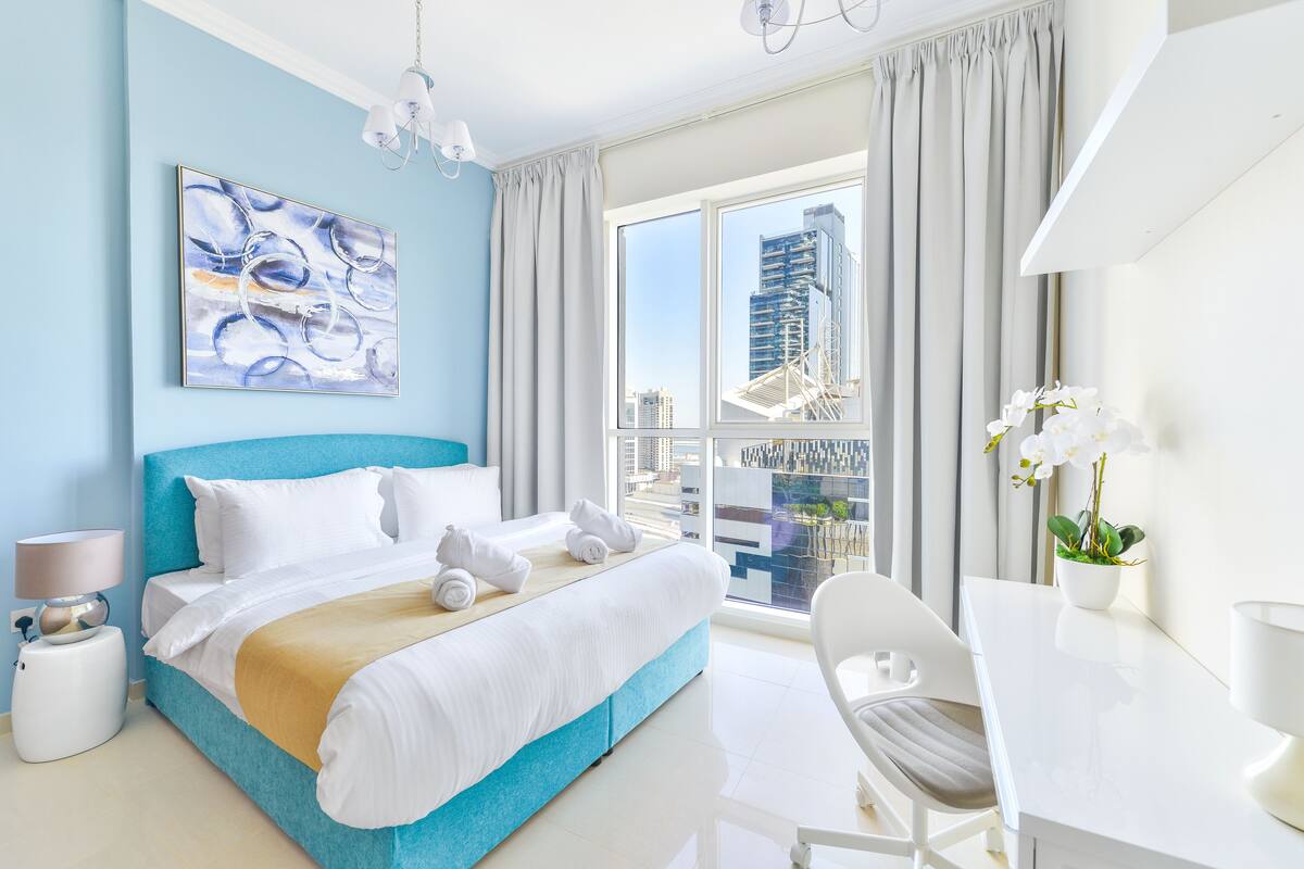 A modern hotel room with a large bed, a desk, and a view of the cityscape.