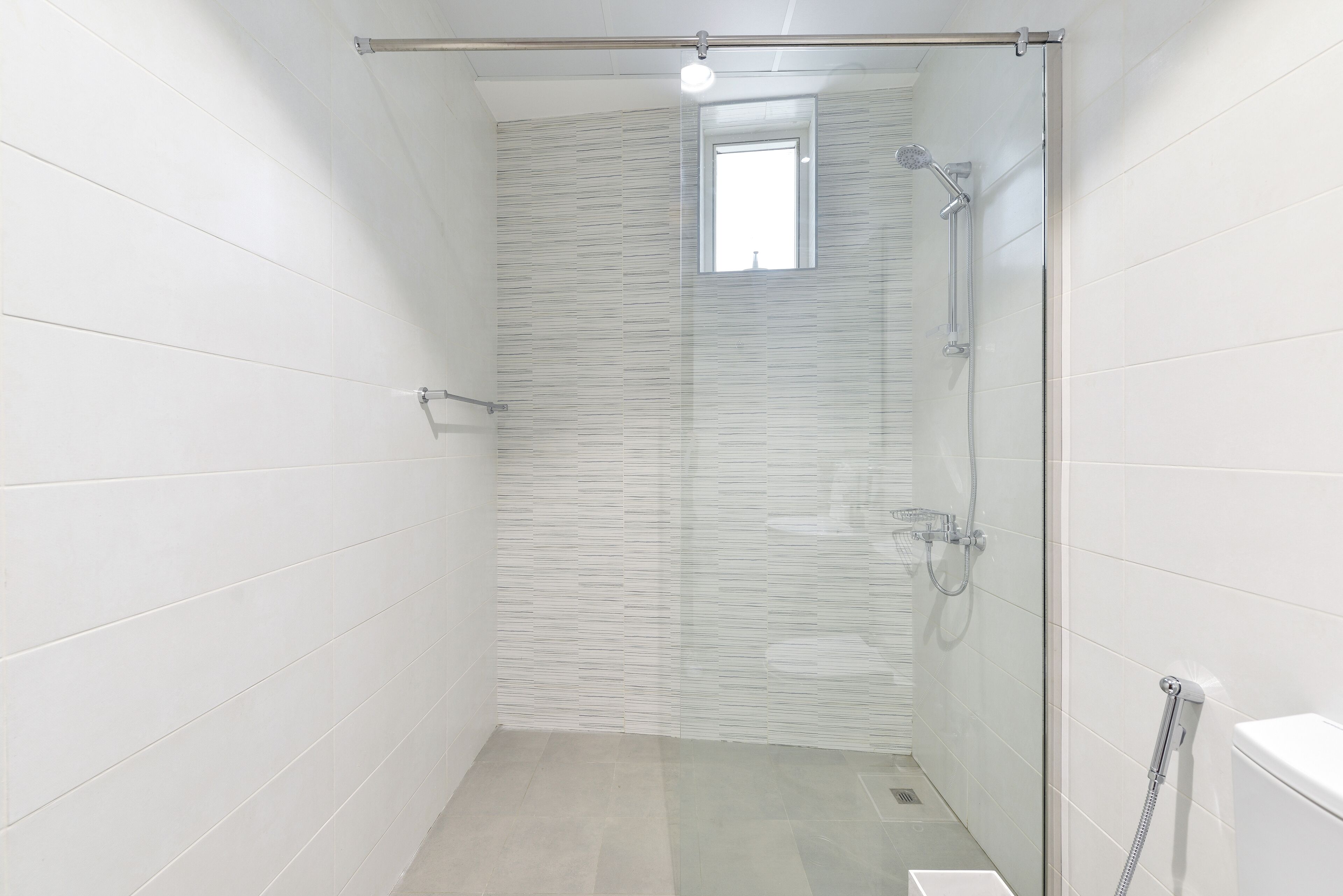 A modern bathroom with a glass shower enclosure, a small window, and a toilet.