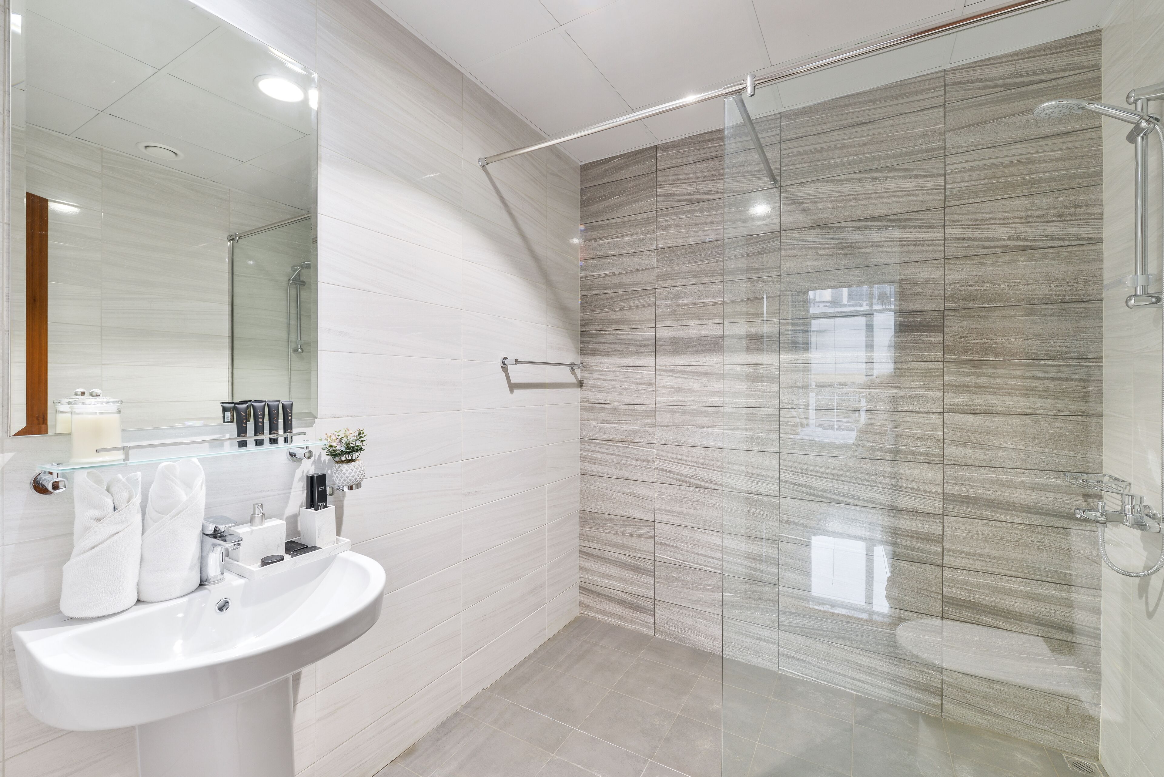 Ein modernes Badezimmer mit einer gläsernen Duschkabine, einem weißen Waschbecken und einem Spiegel darüber.