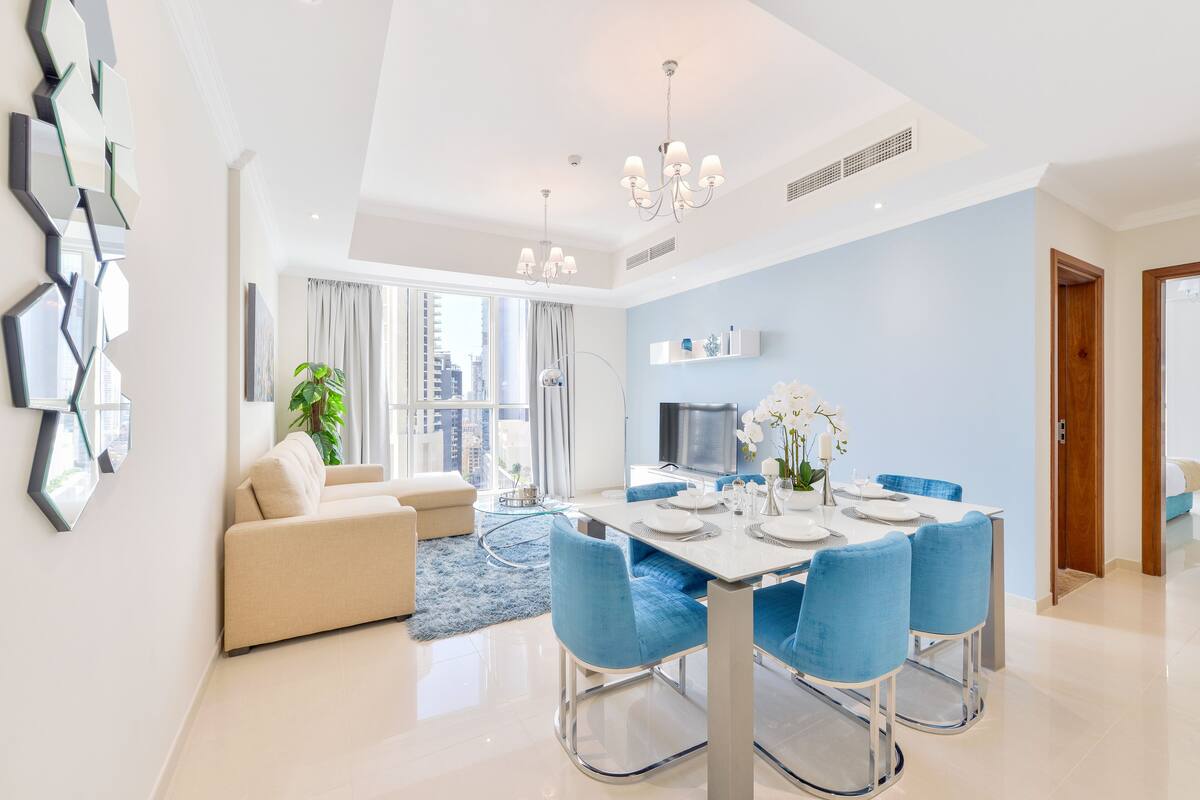 A modern dining area with a white table, blue chairs, and a chandelier.