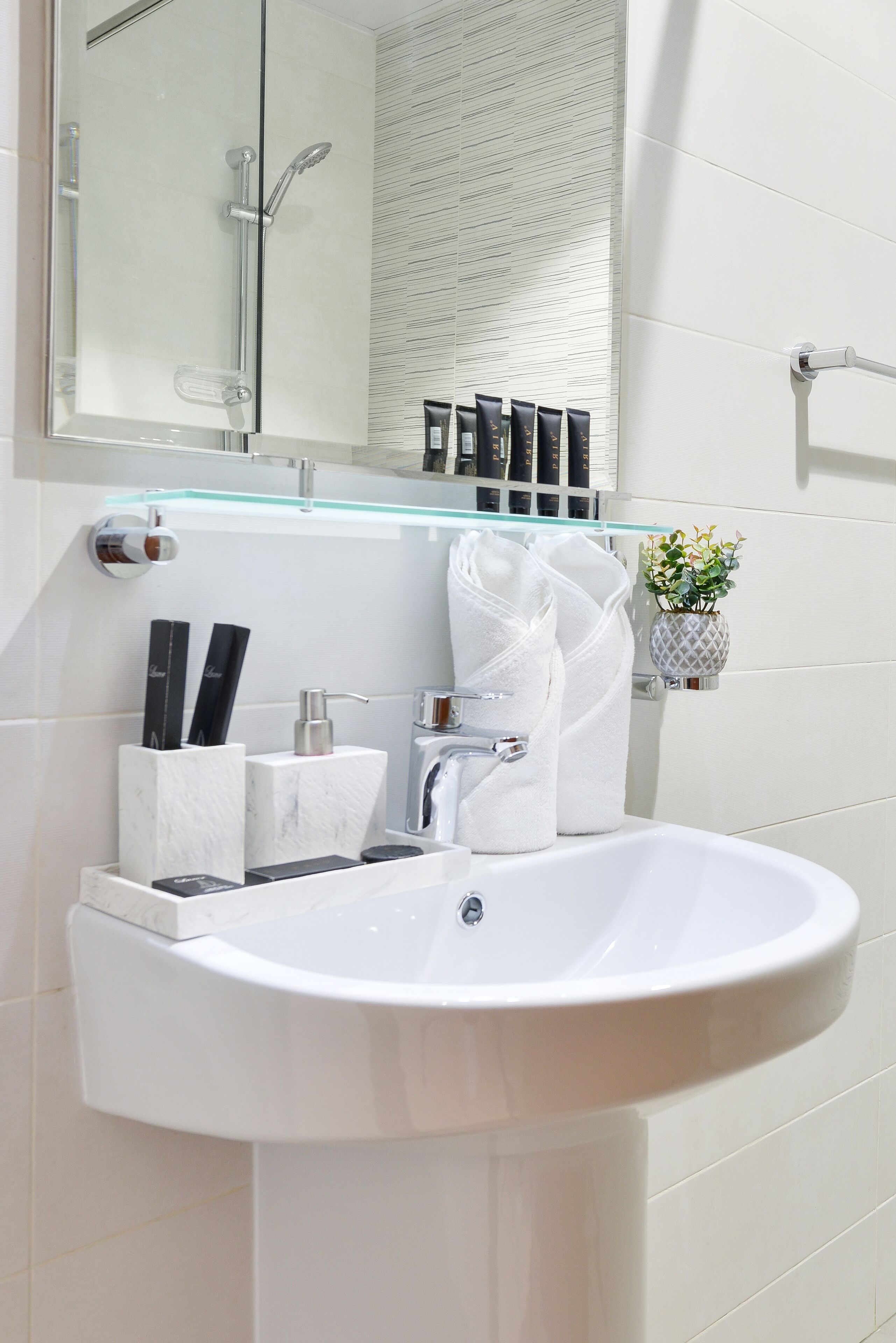 A modern bathroom with a white sink, glass shelf, and a shower area.