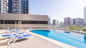 Una piscina en la azotea con sillones reclinables azules y el horizonte de la ciudad al fondo.