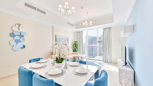 Un comedor moderno con una mesa blanca dispuesta para seis personas, sillas tapizadas en azul y una araña.