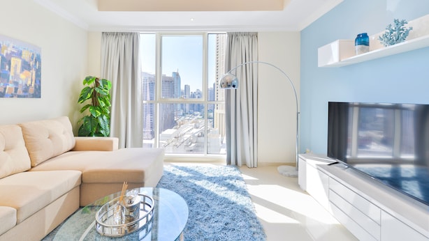 Una sala de estar moderna con sofá, una mesa de centro, televisor y un amplio ventanal con vistas a la ciudad.