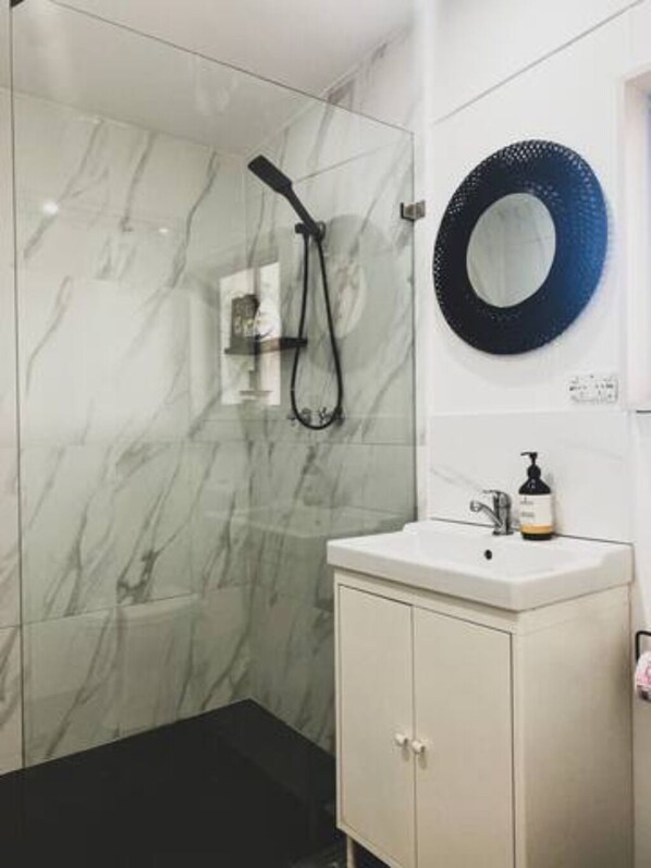 A bathroom with a shower, a sink with a soap dispenser, and a circular mirror on the wall.