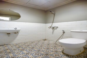 Ein Badezimmer mit weißem Waschbecken, WC und Dusche. Der Boden ist mit einem gemusterten Fliesenbelag versehen.
