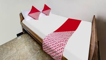 Uma cama de solteiro com colchão branco e colcha estampada em vermelho e branco.