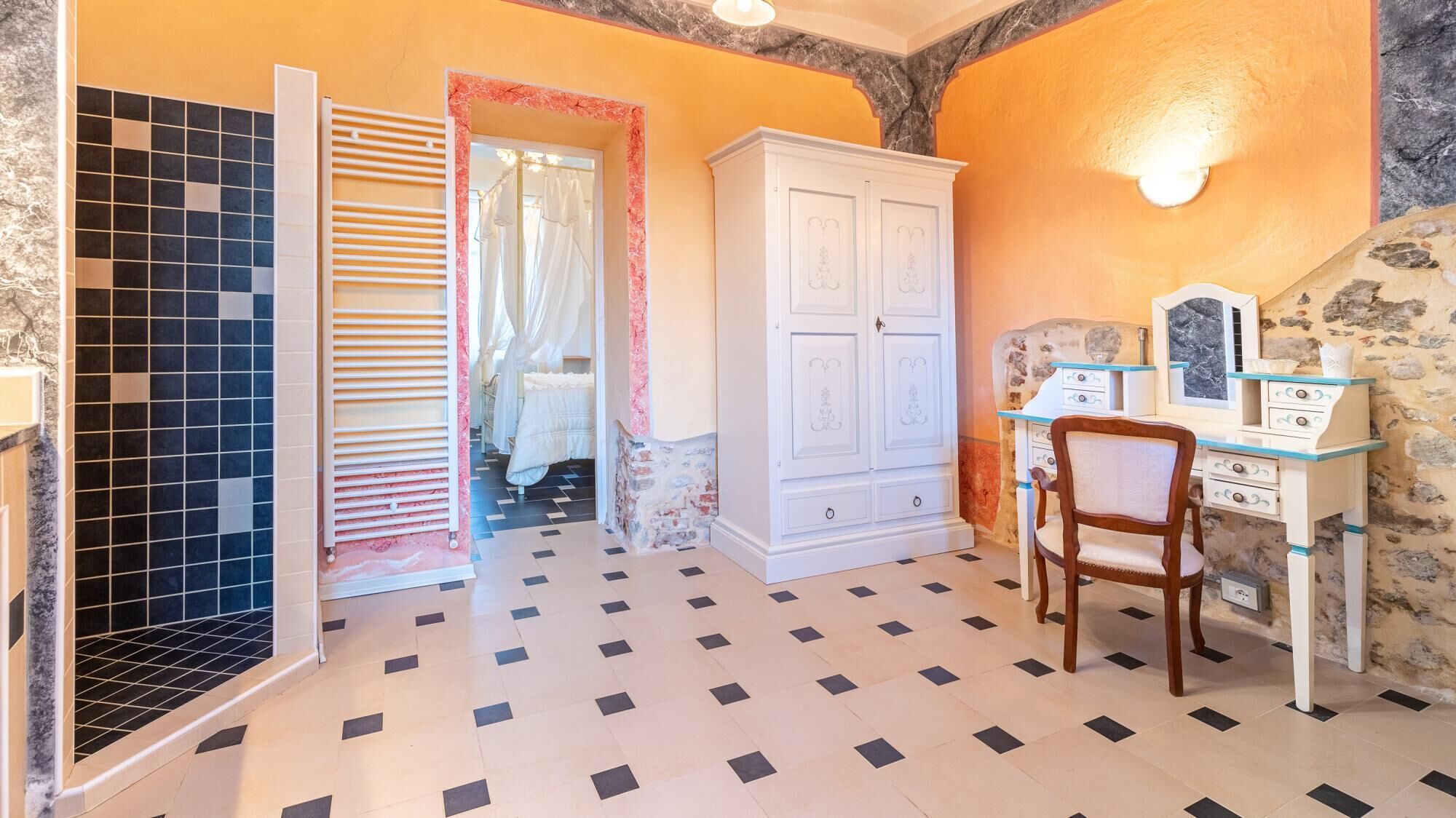 A room with a tiled floor, a white wardrobe, a vanity with a mirror, and a chair.