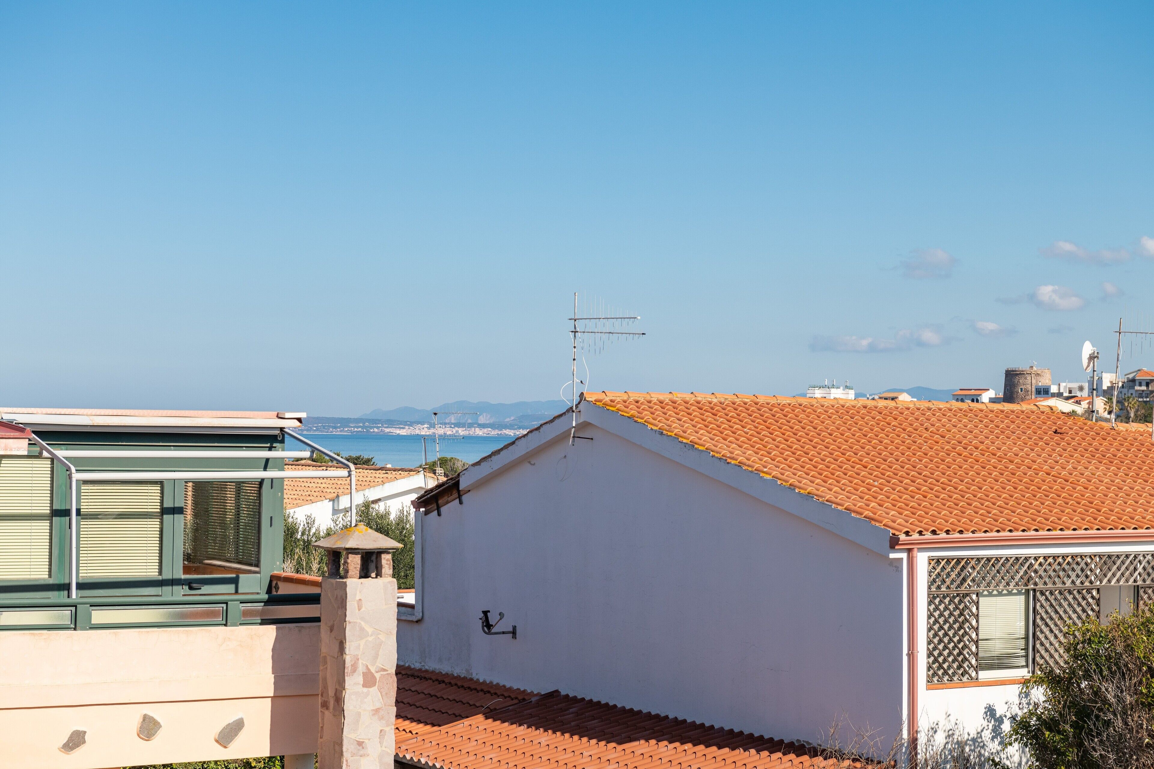 A white building with a tiled roof, a visible antenna, and a view of the sea and distant landscape.