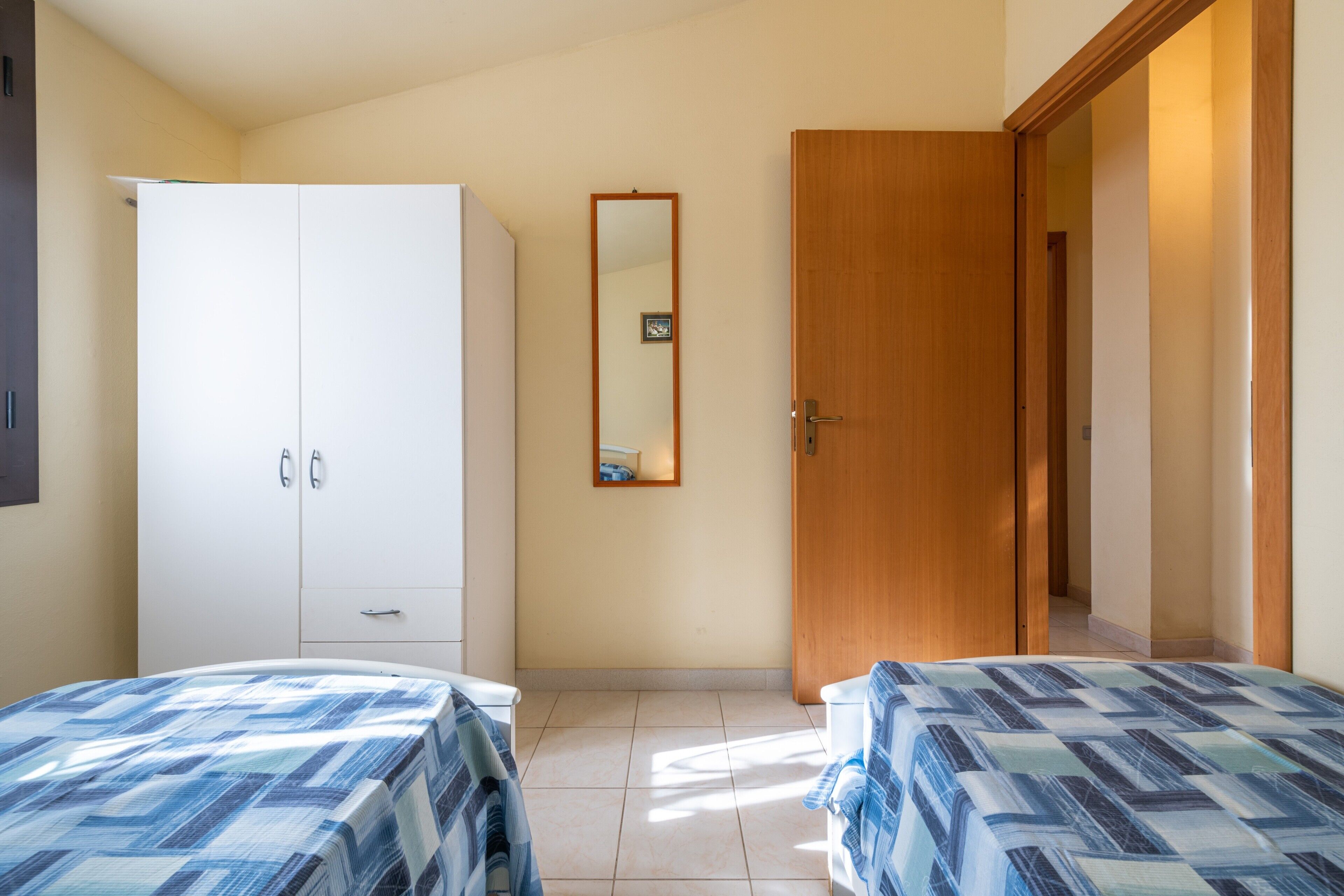 A bedroom with two beds, a wardrobe, a mirror, and a door leading to another room.