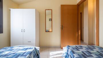 A bedroom with two beds, a wardrobe, a mirror, and a door leading to another room.