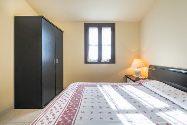 A bedroom with a bed, a wardrobe, a window, and a nightstand with a lamp.