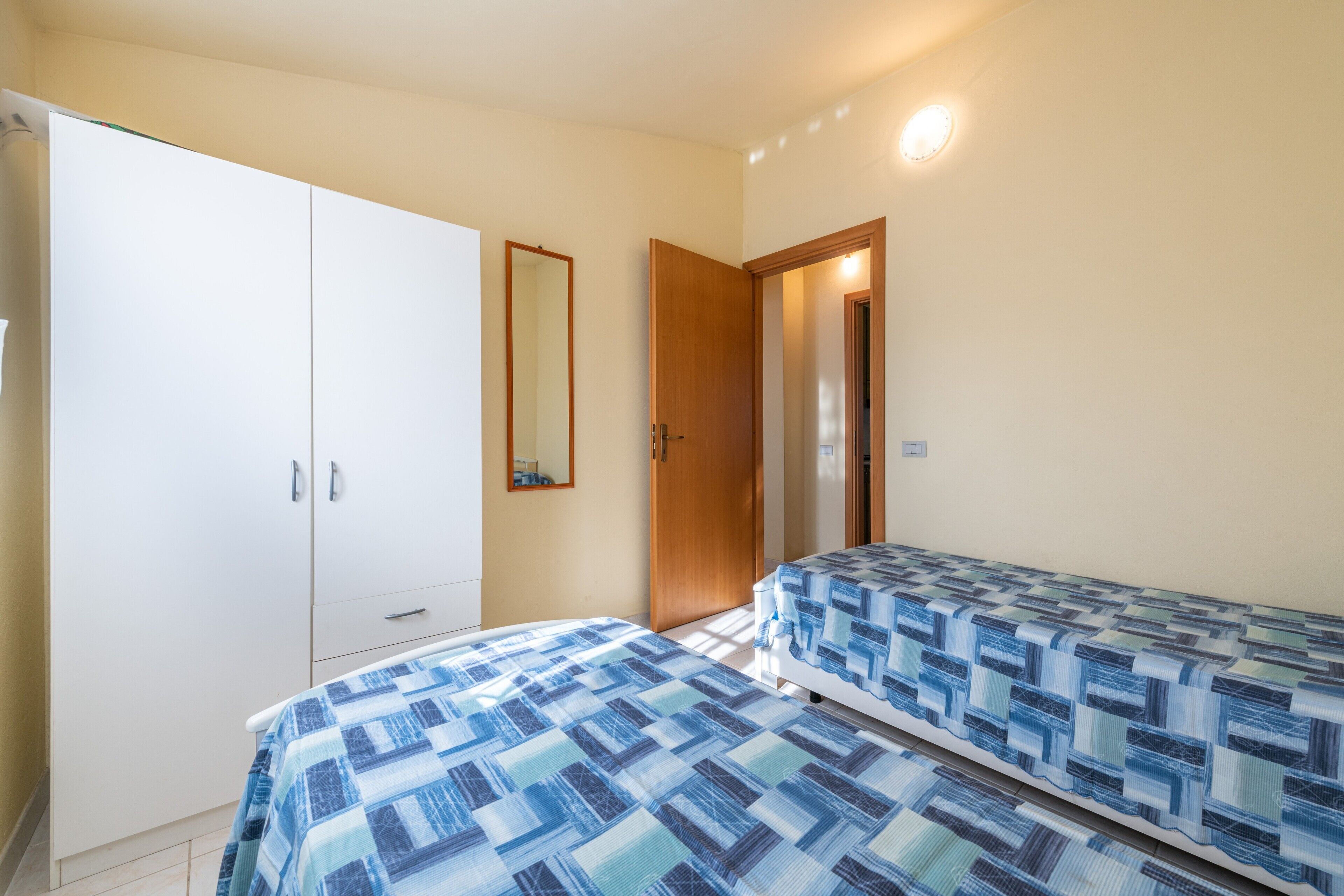 A bedroom with two beds, a wardrobe, a mirror, and a door leading to another room.