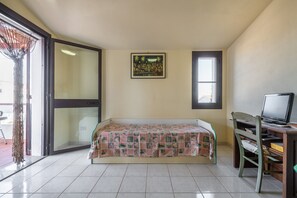 Ein Zimmer mit einem Bett, einem Schreibtisch mit Computer, einem Fenster und einer Tür.