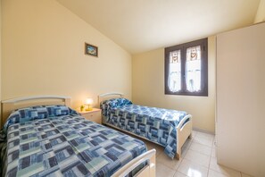 A bedroom with two beds, a nightstand, a window with curtains, and a door. - Vacation Home "Via Mazzini 87" with Private Terrace (Calasetta)