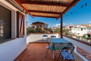 Ein Balkon mit einer Holz-Pergola, einem Tisch mit Stühlen und Blick auf benachbarte Häuser.