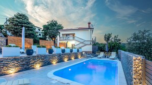 A swimming pool with a stone wall and lounge chairs, surrounded by a stone wall and a building with a red roof. - Apartment First Mary (Matulji)