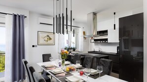 A modern dining area with a white table set for six, black chairs, and a kitchen in the background. - Apartment First Mary (Matulji)