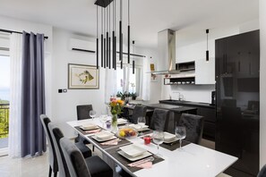 A modern dining area with a white table set for six, black chairs, and a kitchen in the background. - Apartment First Mary (Matulji)