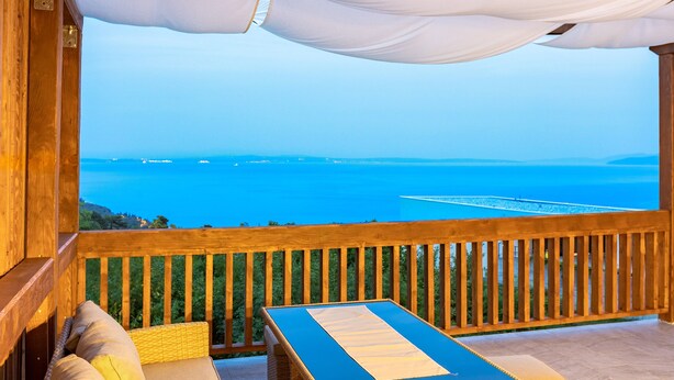 A wooden deck with a table and chairs, overlooking a coastal view with a clear sky. - Apartment First Mary (Matulji)