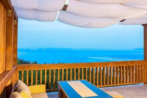 Une terrasse en bois avec une table et des chaises, offrant une vue sur la côte et un ciel dégagé.