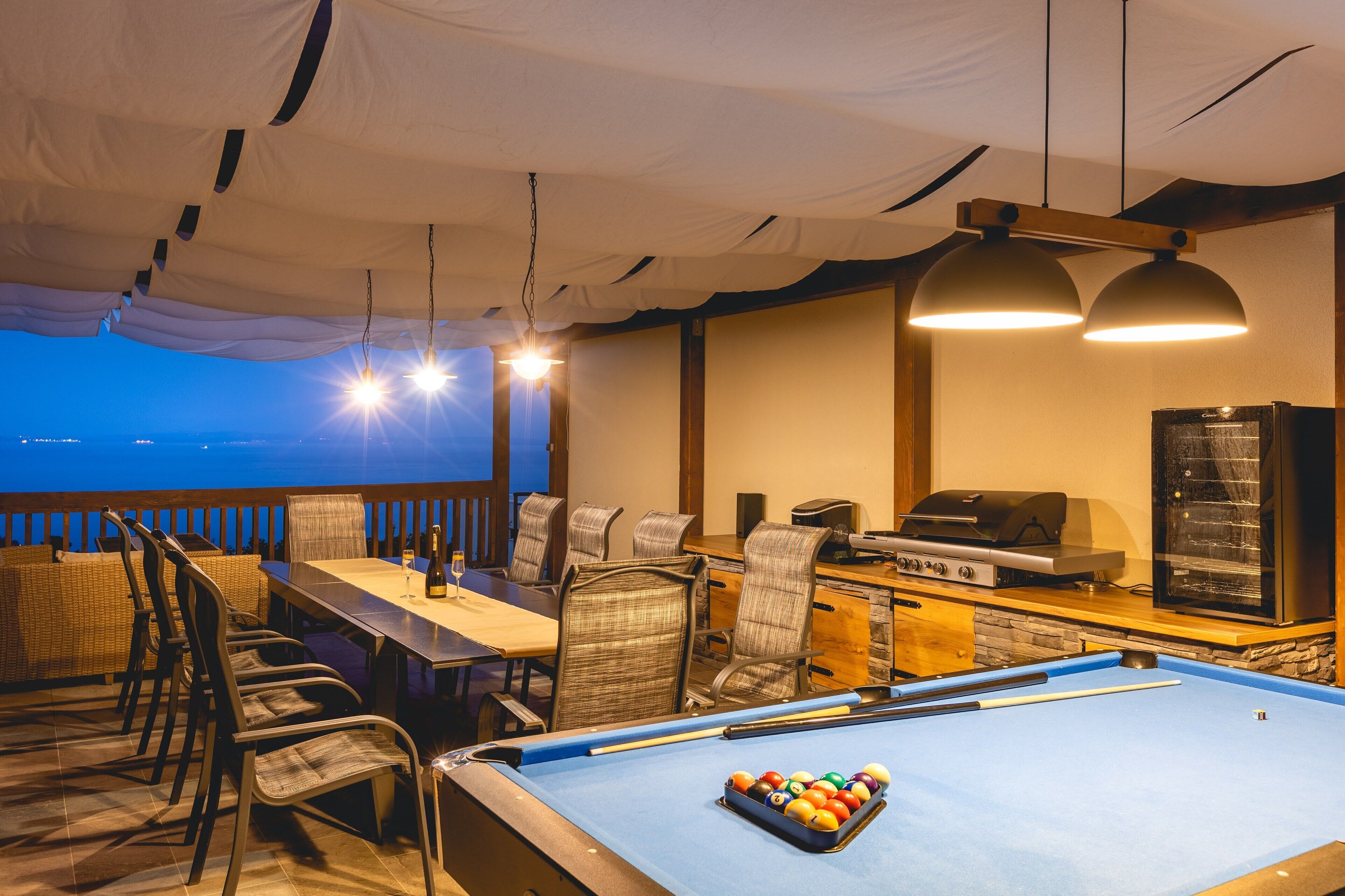 A pool table with billiard balls, a grill, and a dining area with chairs and a table.