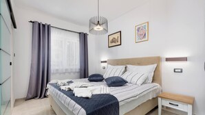 A modern bedroom with a bed, bedside tables, a hanging light fixture, and artwork on the walls. - Apartment First Mary (Matulji)