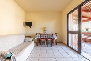 Une pièce comprenant un canapé, une table à manger avec des chaises, un téléviseur fixé au mur et une grande fenêtre donnant sur un beau paysage.