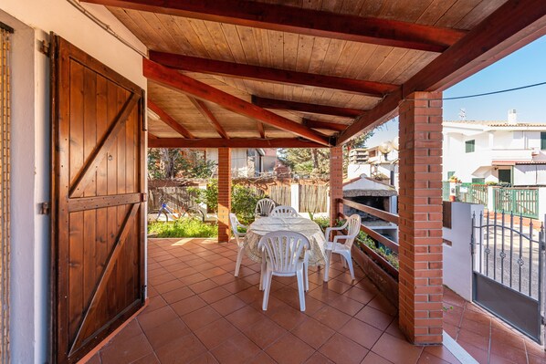 Une terrasse couverte avec une table et des chaises, une porte en bois et un mur en briques.