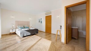 Une chambre à coucher comprenant un lit, une table de chevet et un bureau avec une chaise. Une porte donne accès à une salle de bain.