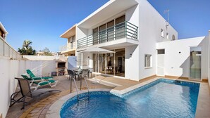 Une maison moderne à deux étages, dotée d’une piscine, de mobilier d’extérieur et d’un balcon.