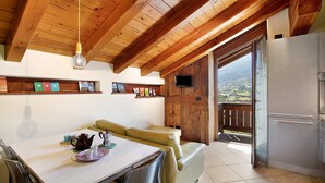 Une cuisine avec des poutres en bois, une table à manger avec des chaises, un canapé et une vue sur l’extérieur par une porte ouverte.