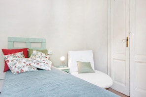 Un lit avec des coussins à motifs floraux, une lampe de chevet et une porte blanche.