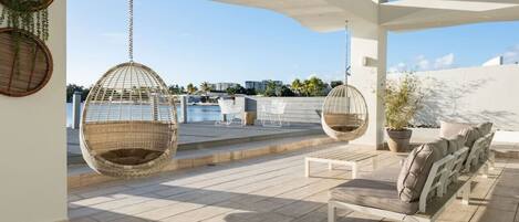A rooftop terrace with hanging chairs, a lounge area, and a view of the city skyline.