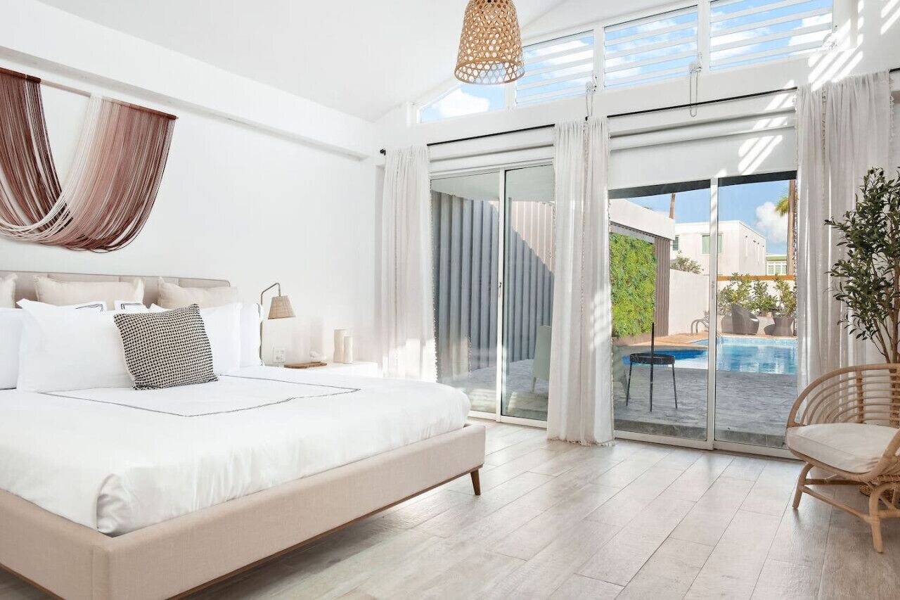Ein geräumiges Schlafzimmer mit einem großen Bett, einer Schiebetür zu einem Poolbereich und einem Korbsessel.