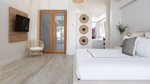 A modern bedroom with a large bed, a television mounted on the wall, a wicker chair, and a sliding glass door leading to a balcony.