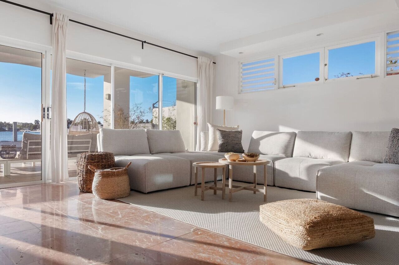 Un salon moderne avec un grand canapé d’angle, une petite table ronde et une vue sur la mer grâce à de grandes fenêtres.