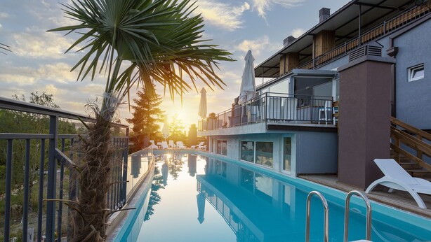 Une piscine avec des chaises longues, un palmier et un bâtiment doté de balcons.