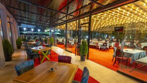 Un espace de restauration intérieur avec des tables et des chaises, une moquette rouge et un mur de verre donnant sur l’extérieur.