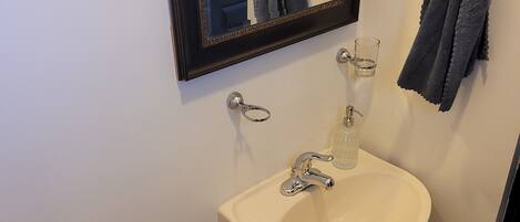A bathroom with a white sink, a mirror, a towel ring, and a toilet.