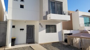 Un bâtiment moderne à deux étages, avec une porte grise portant le numéro 455 et un balcon doté de rampes en métal.