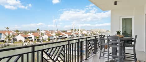 A balcony with a view of a marina, a dining area with chairs and a table, and a cityscape in the background.