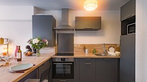 A modern kitchen with dark cabinetry, a wooden countertop, a built-in oven, and a stainless steel sink. - Cosy apartment with large balcony and private parking (Lorient)