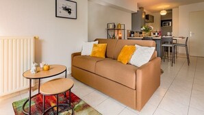 A modern living room with a brown sofa, a small round table, and a colorful rug. - Cosy apartment with large balcony and private parking (Lorient)
